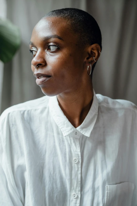 a woman in a white shirt looking out a window, by Dulah Marie Evans, wearing a white button up shirt, shaved hair, nuri iyem, plain background