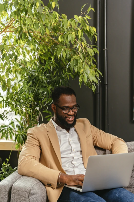 a man sitting on a couch using a laptop, pexels contest winner, renaissance, brown skin man with a giant grin, next to a plant, professional profile picture, office background