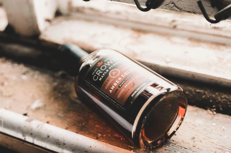 a bottle of alcohol sitting on a window sill, by Emma Andijewska, pexels contest winner, baroque, on a wooden desk, black and auburn colour pallet, close-up product photo, ground broken