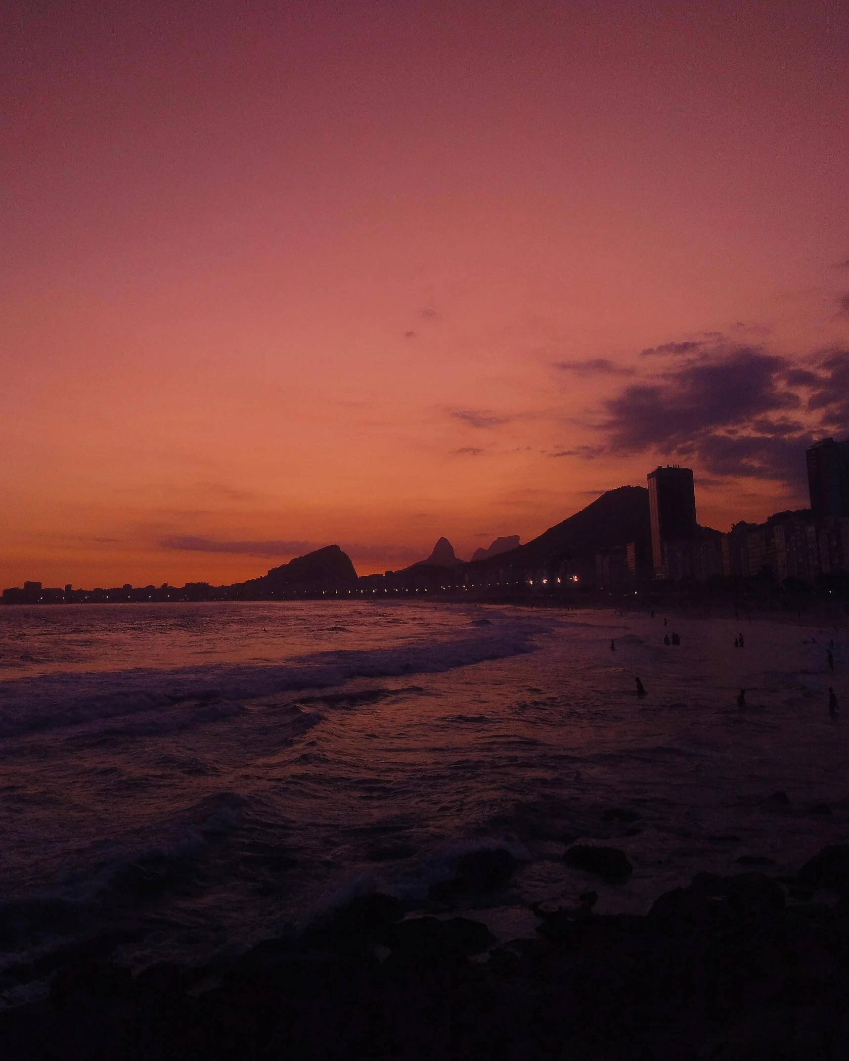 a group of people standing on top of a beach next to the ocean, an album cover, by Elsa Bleda, pexels contest winner, city sunset night, window with rio de janeiro view, ☁🌪🌙👩🏾, purple hues