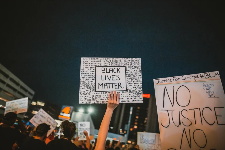a person holding a sign that says black lives matter, a black and white photo, by Julia Pishtar, trending on unsplash, night photo, multiple stories, center of picture, instagram post