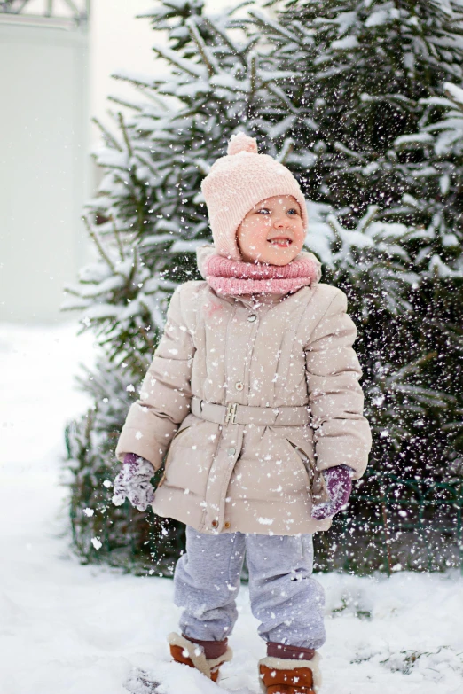 a little girl that is standing in the snow, a picture, with a tree in the background, wearing jacket, promo image, catalog photo