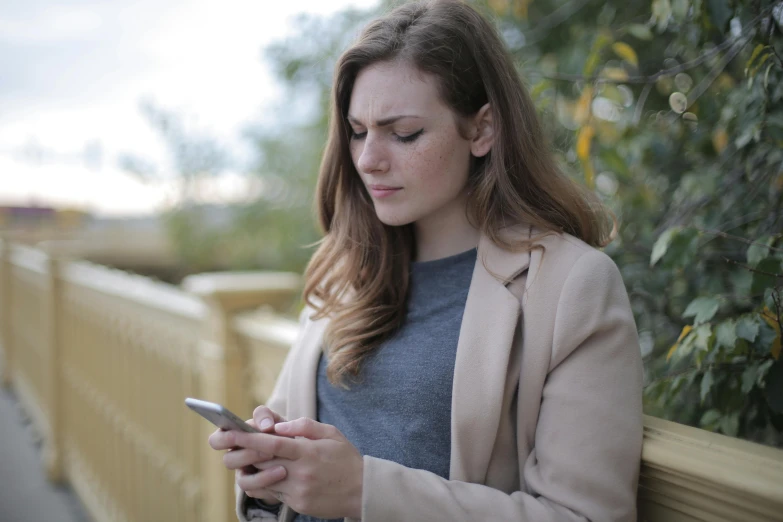 a woman is looking at her cell phone, trending on pexels, her gaze is downcast, brown, grey, outside