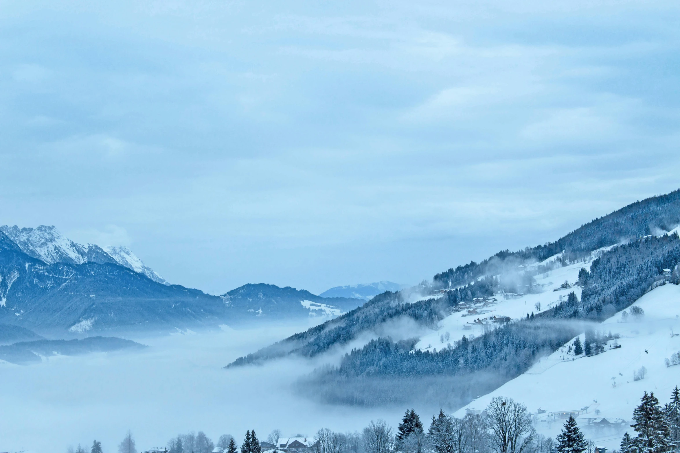 a group of people riding skis down a snow covered slope, by Matthias Weischer, pexels contest winner, romanticism, cyan fog, distant town in valley and hills, landscape wallpaper, white and blue