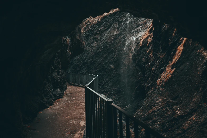 a walkway in a cave with a waterfall coming out of it, inspired by Elsa Bleda, pexels contest winner, natural prison light, thumbnail, black, volcanic