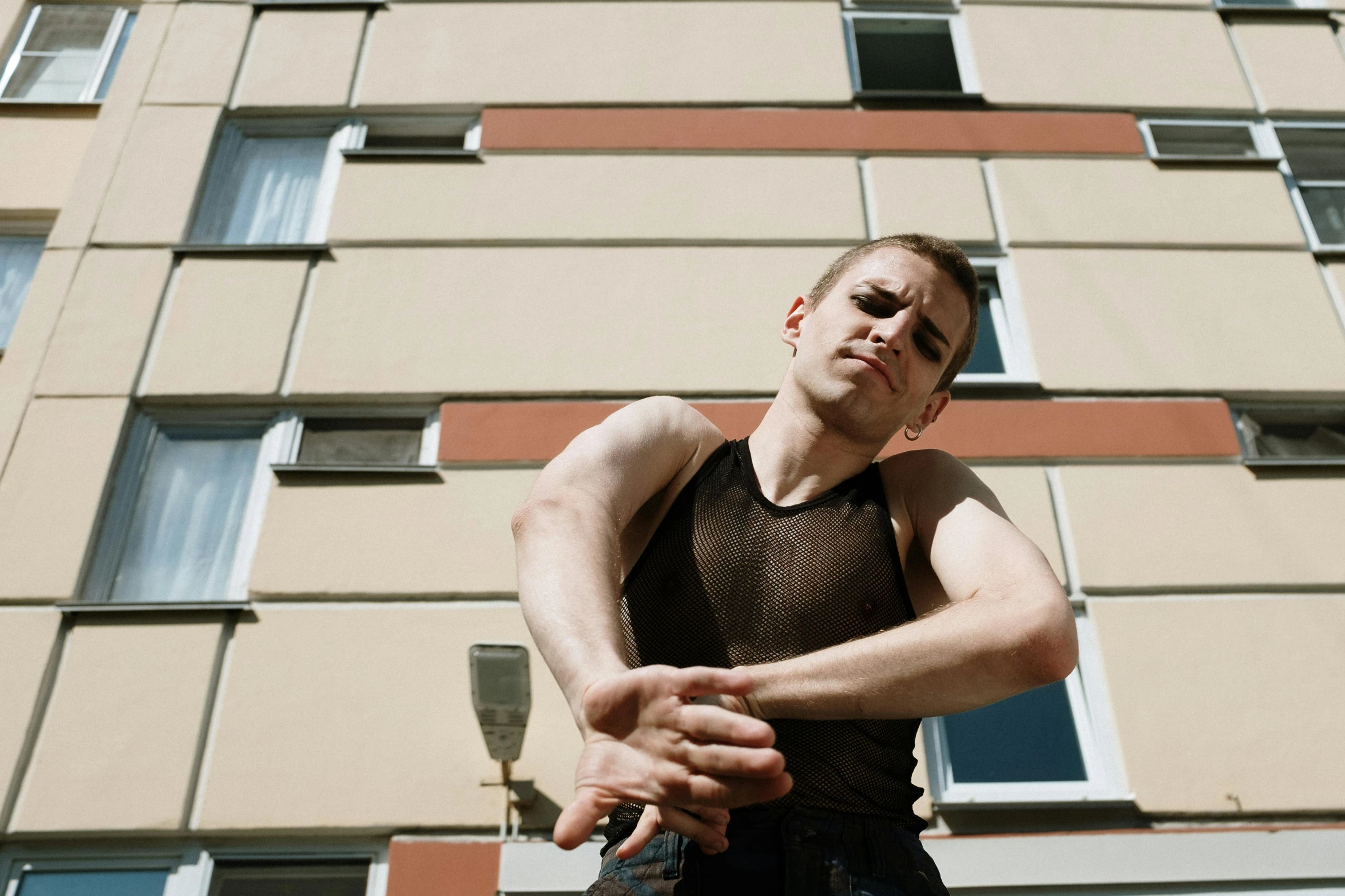 a man standing in front of a tall building, by Attila Meszlenyi, unsplash, bauhaus, wearing a vest top, vitalik buterin, posing ready for a fight, standing outside a house