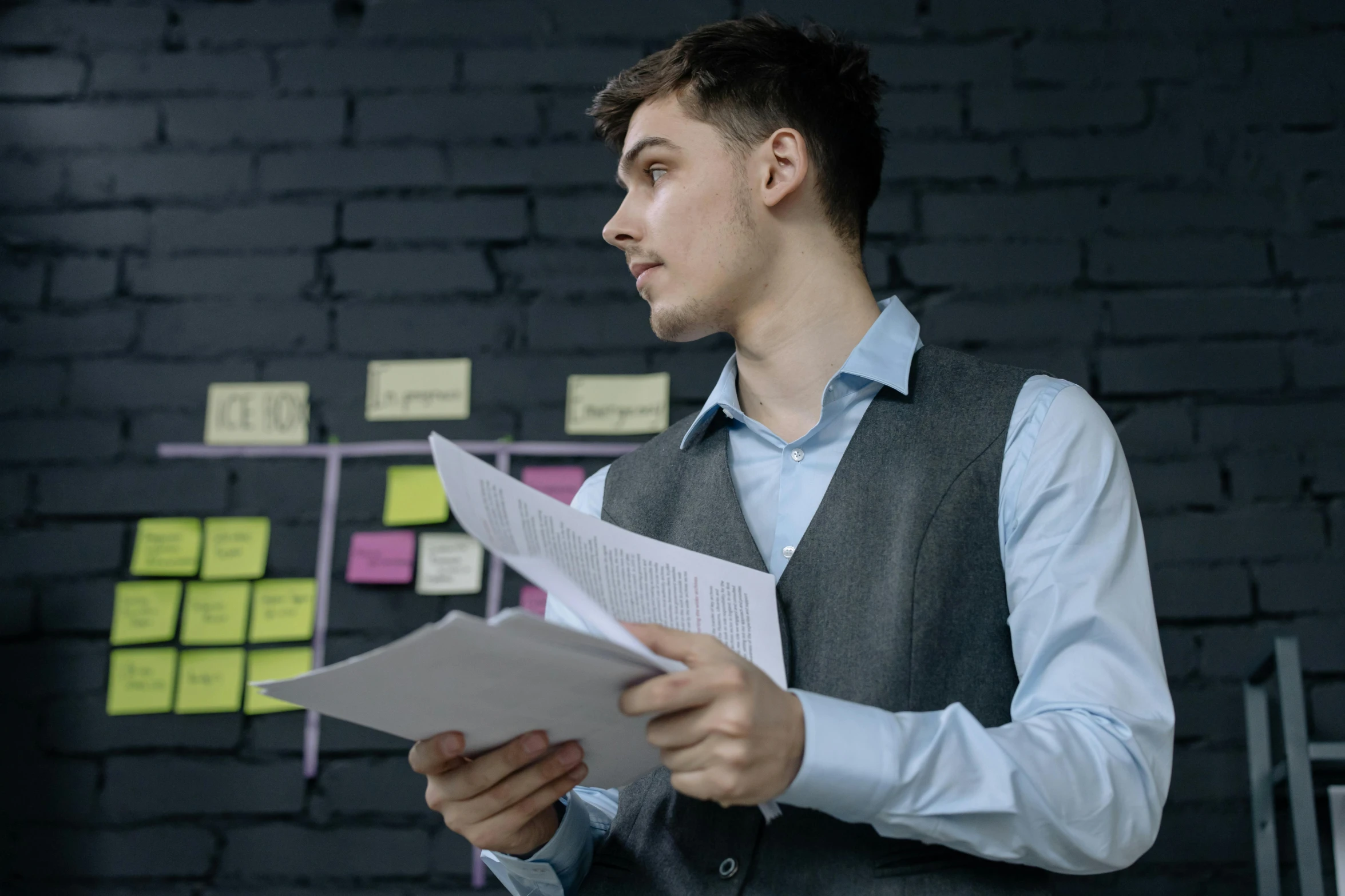 a man standing in front of a brick wall holding a piece of paper, pexels contest winner, working in an office, profile image, thumbnail, background image