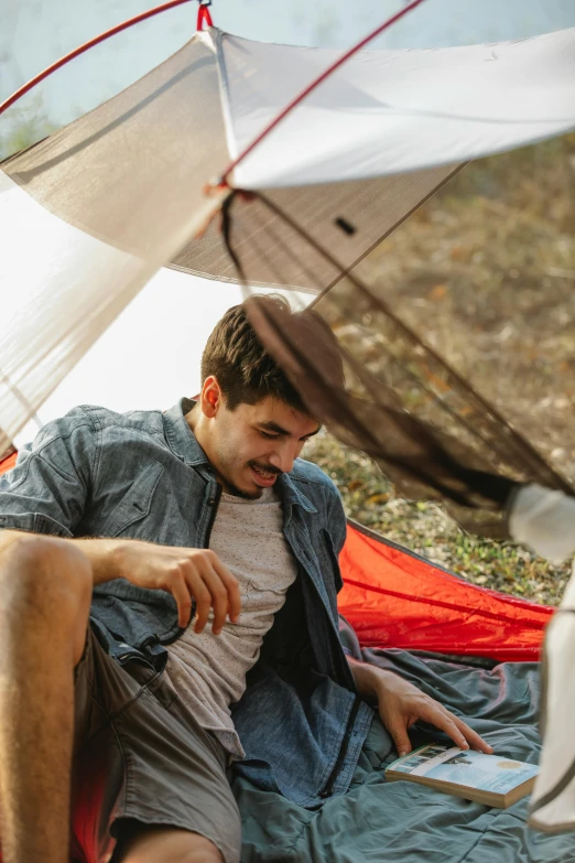 a man sitting in a tent using a laptop, by Jessie Algie, trending on unsplash, renaissance, drenched clothing, laying under a tree on a farm, a man wearing a backpack, adam ondra