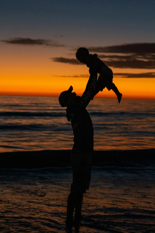 a silhouette of a person holding a child at the beach, a picture, by Robbie Trevino, 8k photo, various posed, f / 2 0, predawn