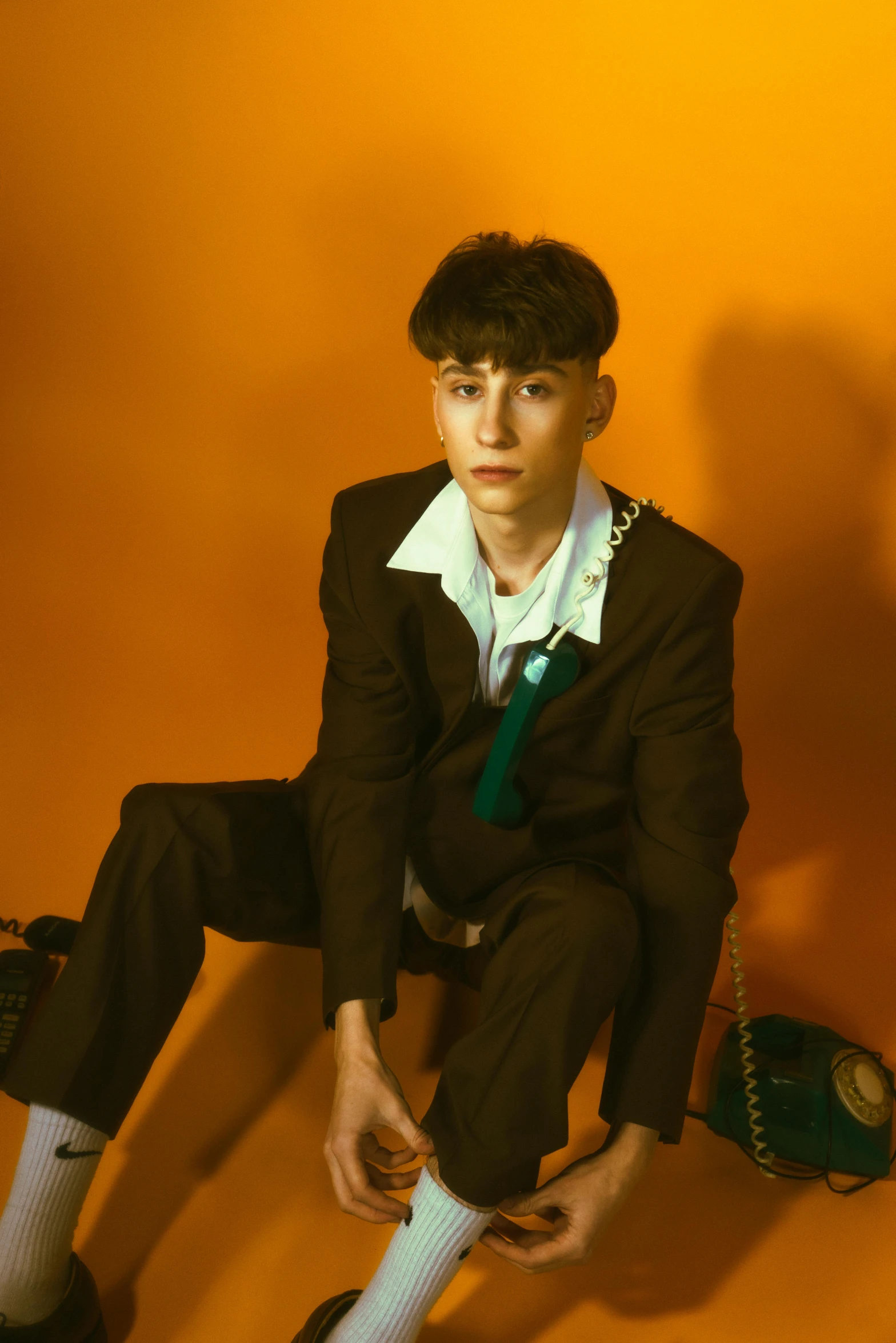 a man in a suit and tie sitting on a floor, an album cover, trending on pexels, declan mckenna, jean deville, wearing school uniform, shot at golden hour