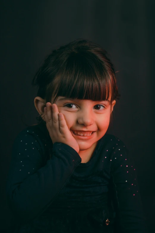 a little girl smiling with her hands on her face, a character portrait, by Leo Michelson, pexels contest winner, dark. studio lighting, portrait of a small, led, hand on cheek