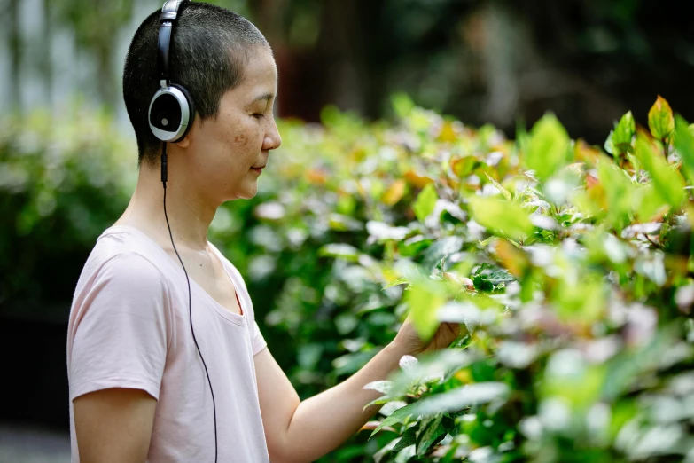 a person standing in front of a bush with headphones on, inspired by Song Xu, happening, biodiversity all round, garden environment, close up of iwakura lain, tapping in to something greater