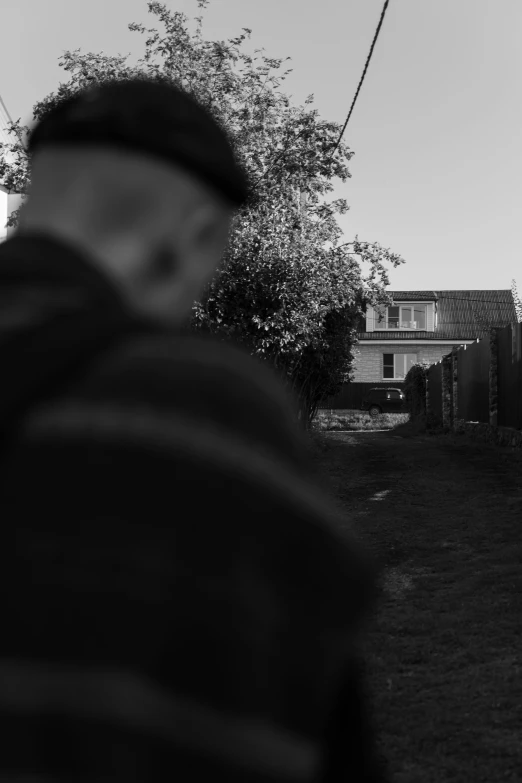 a black and white photo of a man walking down a street, a black and white photo, unsplash, realism, people looking at a house, suburb, hunting, low dutch angle