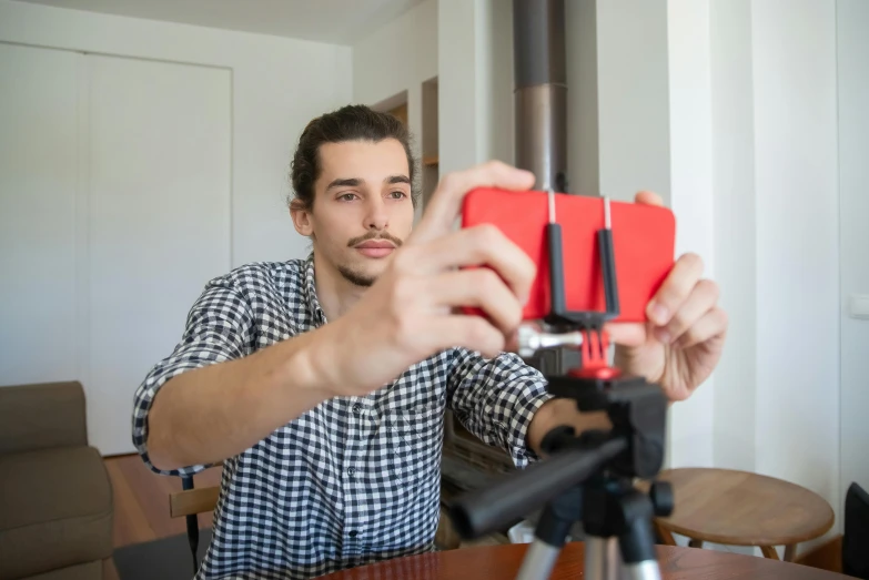 a man taking a picture of himself with a camera, shutterstock, video art, light stubble with red shirt, tripod, at home, looking at his phone