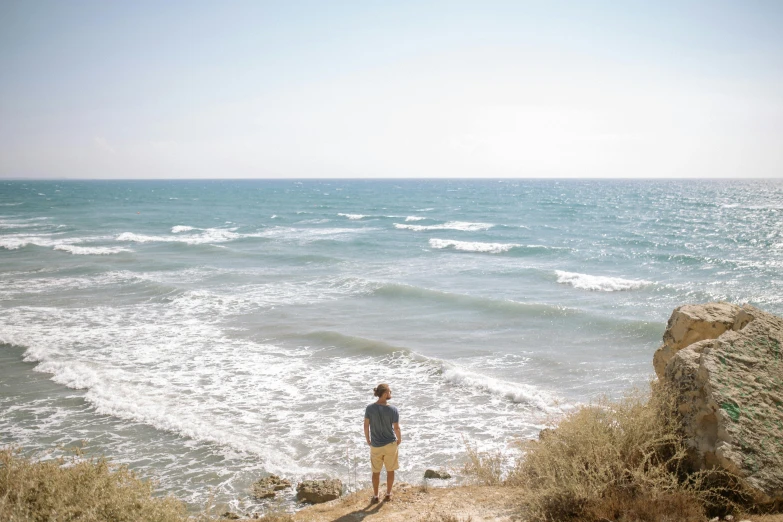 a man standing on top of a cliff next to the ocean, unsplash, israel, soft shade, sparsely populated, chillwave