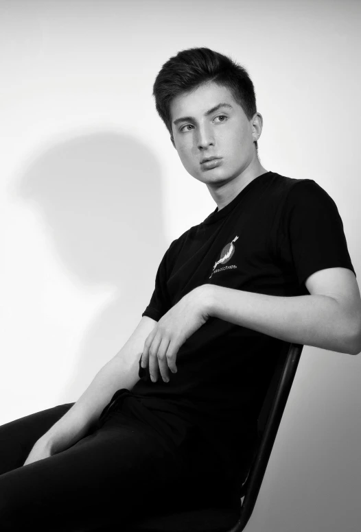 a black and white photo of a man sitting in a chair, inspired by Tommaso Redi, wearing black tshirt, male teenager, pose 4 of 1 6, ismail