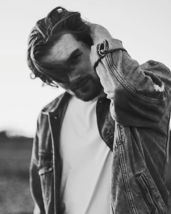 a man standing in a field talking on a cell phone, a black and white photo, pexels contest winner, portrait of a rugged young man, hozier, wearing a jeans jackets, depressed dramatic bicep pose