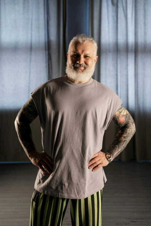 a man standing in a room with his hands on his hips, a tattoo, inspired by Lajos Vajda, gray hair and beard, wearing a muscle tee shirt, big wide broad strong physique |, portrait photo