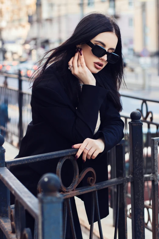 a woman leaning on a fence talking on a cell phone, a picture, by Julia Pishtar, trending on pexels, fashion model in sunglasses, slicked black hair, anna nikonova aka newmilky, black coat