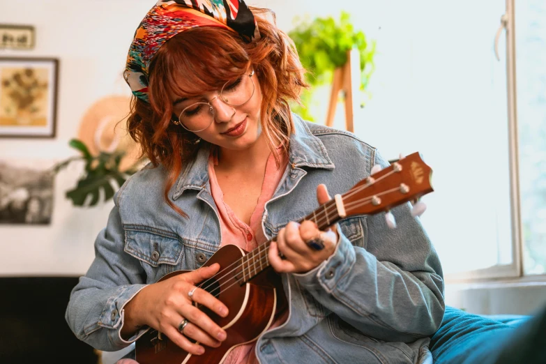a woman sitting on a couch playing a guitar, by Julia Pishtar, pexels, wearing a headband, a redheaded young woman, ukulele, avatar image