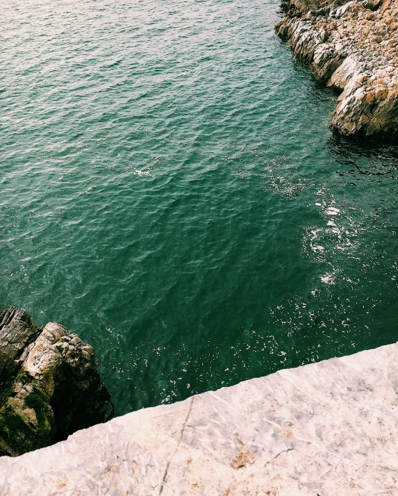 a person jumping off a cliff into a body of water, an album cover, inspired by Elsa Bleda, trending on unsplash, green tonalities, ((rocks)), cinq terre, trending on vsco