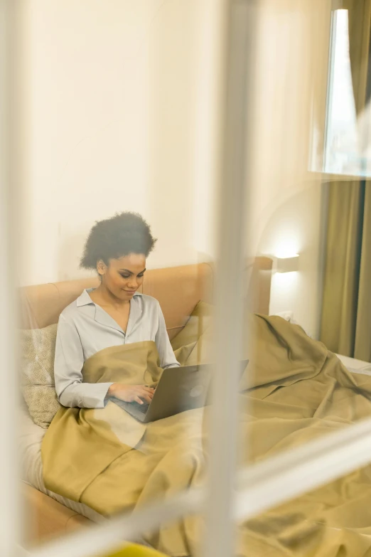 a woman sitting on a bed using a laptop, trending on pexels, happening, golden hues, translucent, african american woman, hotel room