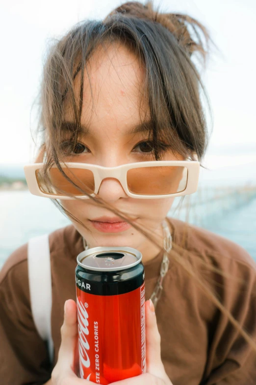 a woman holding a can of coke in front of her face, by Jang Seung-eop, pexels contest winner, with square glasses, ulzzang, pokimane, distant photo