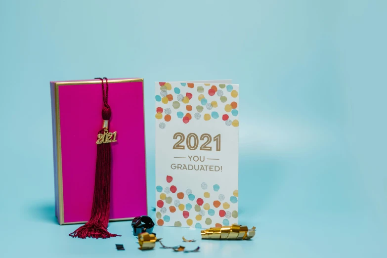 a book sitting on top of a table next to a graduation cap, a picture, trending on pexels, happening, greeting card, background image, tassels, standing in gold foil