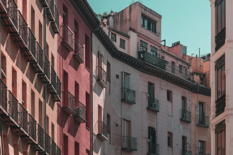 a couple of buildings that are next to each other, a colorized photo, by Luis Molinari, pexels contest winner, hyperrealism, soft red tone colors, balconies, teal and pink, madrid