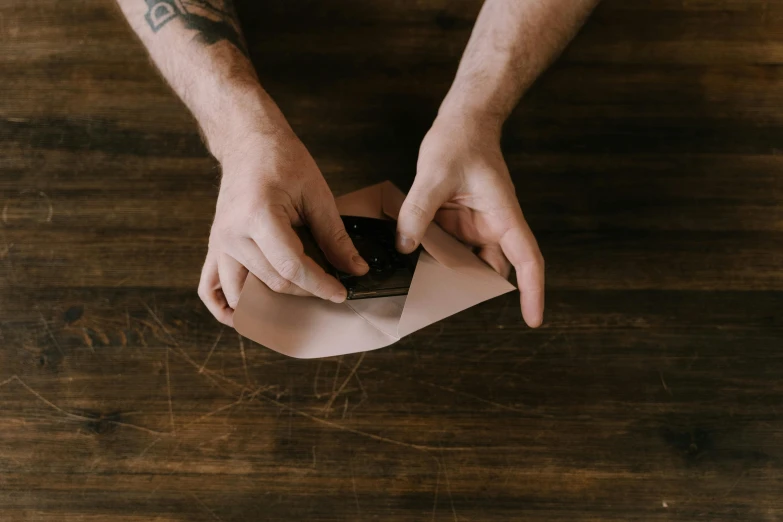 a man cutting a piece of paper on top of a wooden table, by Andrew Stevovich, pexels contest winner, packaging, folds, brown, gif
