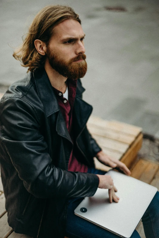 a man sitting on a bench with a laptop, a character portrait, trending on pexels, with a beard and a black jacket, long ginger hair, writing in journal, wearing leather