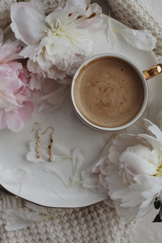 a cup of coffee sitting on top of a white plate, a still life, by Lucia Peka, trending on pexels, romanticism, long earrings, gold flaked flowers, milk and mocha style, detailed product image