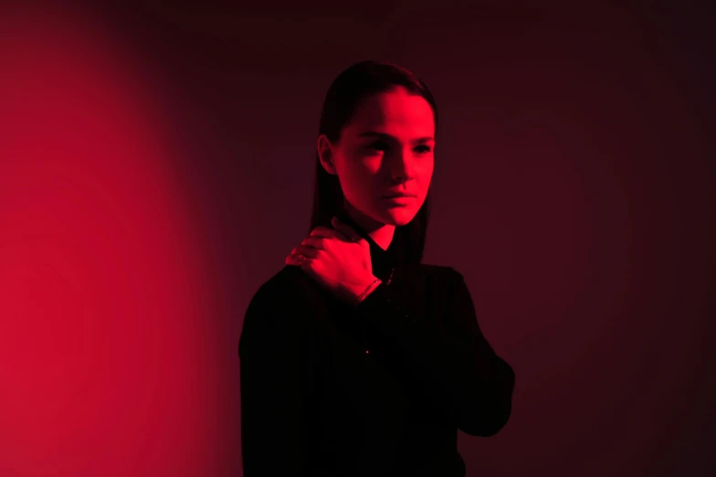 a woman standing in front of a red light, by Emma Andijewska, antipodeans, portrait of natalie portman, dark. studio lighting, aurora aksnes, promotional image