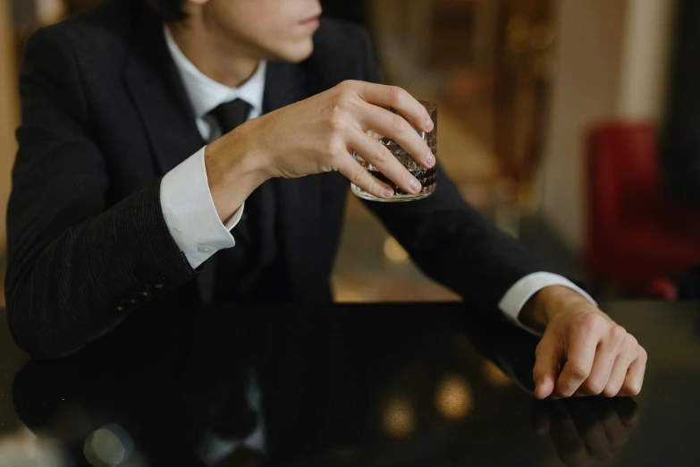 a man in a suit sitting at a table, trending on pexels, bartending, black jewellery, thumbnail, teaser