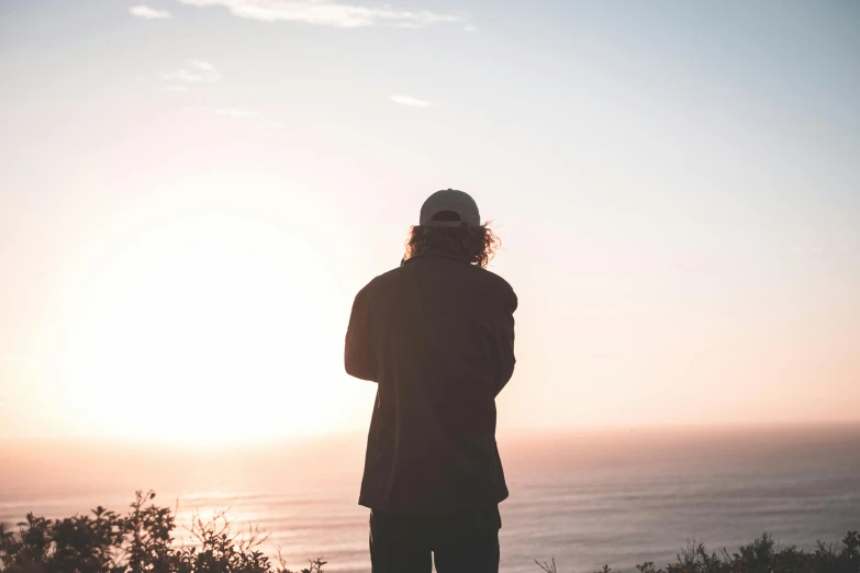 a man standing on top of a hill next to the ocean, pexels contest winner, looking off into the sunset, profile picture, casually dressed, faded glow