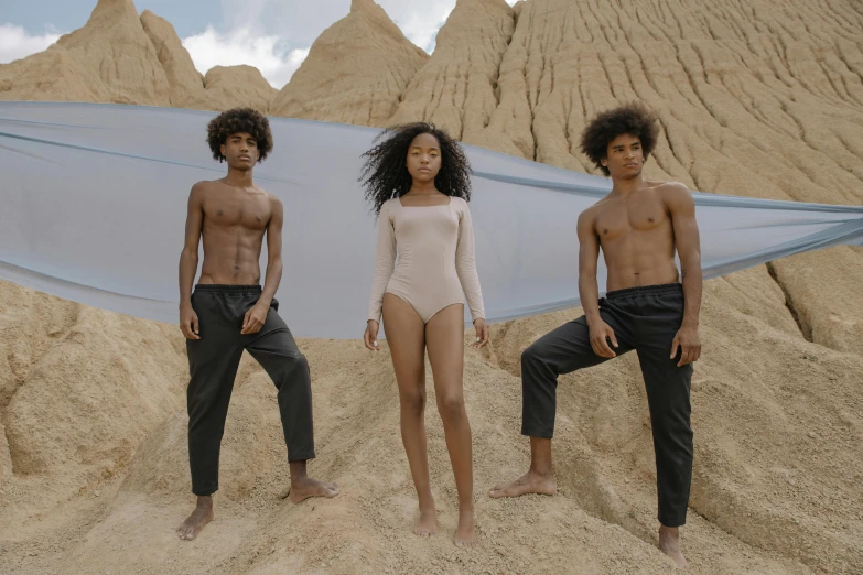 a couple of people that are standing in the sand, inspired by Vanessa Beecroft, pexels contest winner, afrofuturism, three futuristic princes, wearing leotard, long afro hair, promotional image