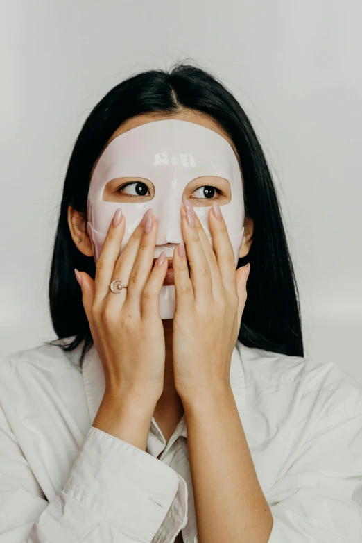 a woman covering her face with a sheet mask, inspired by Marina Abramović, trending on pexels, on clear background, asian woman, square face, silicone skin