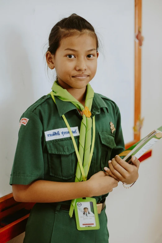 a young girl in a green uniform holding a toothbrush, inspired by Ruth Jên, boy scout troop, holding notebook, nivanh chanthara, looking towards the camera