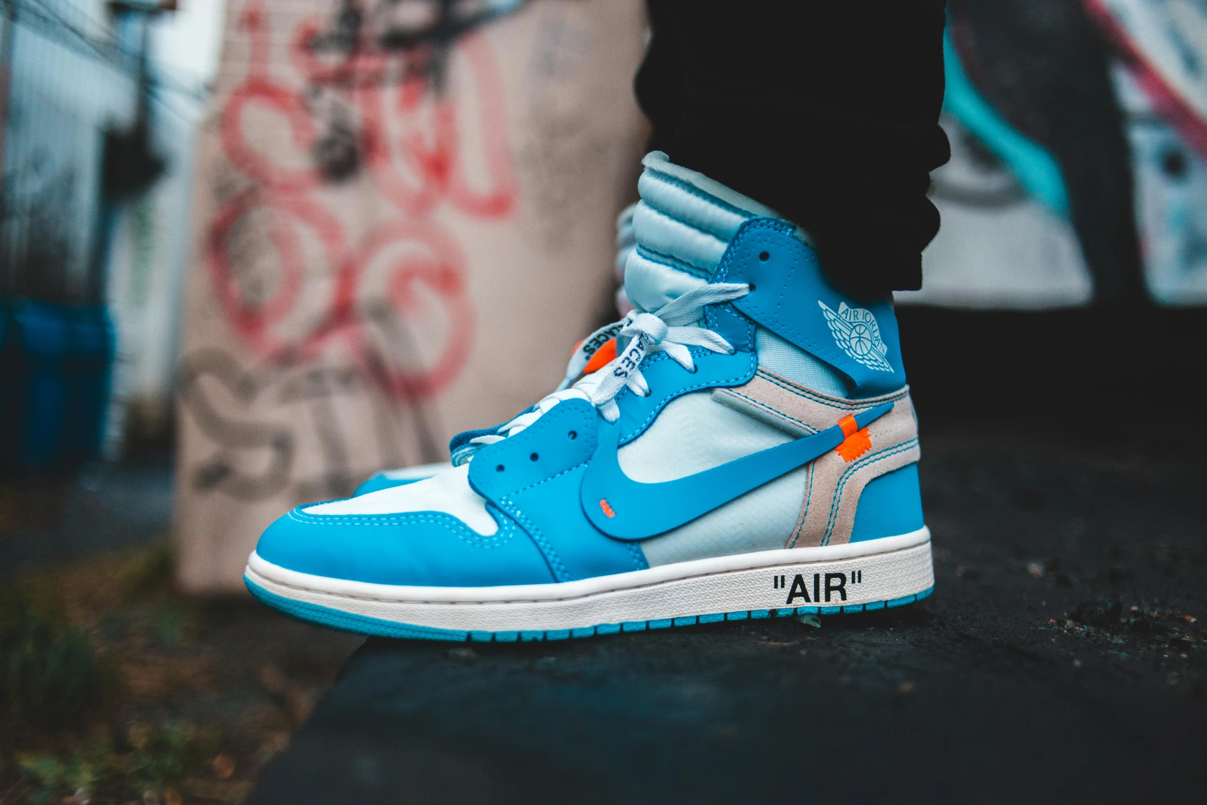 a person standing next to a wall with graffiti on it, trending on pexels, graffiti, air jordan 1 high, blue!! with orange details, off white, flat lay