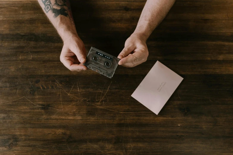 a man holding a cassette on top of a wooden table, connection rituals, plastic wrap, thumbnail, inspect in inventory image