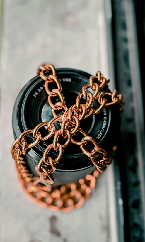 a close up of a camera with a chain around it, trending on pexels, process art, reflections in copper, high resolution product photo, panoramic shot, taken with sony alpha 9