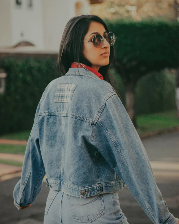 a woman in a denim jacket is walking down the street, an album cover, pexels contest winner, chile, profile image, vintage clothing, mia khalifa