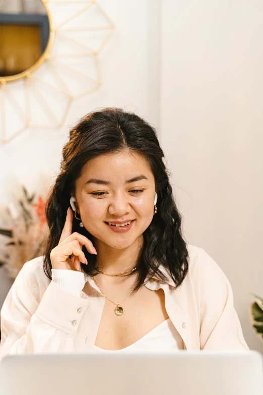 a woman sitting in front of a laptop talking on a cell phone, inspired by helen huang, trending on pexels, wearing ornate earrings, young cute wan asian face, wearing a linen shirt, promo image