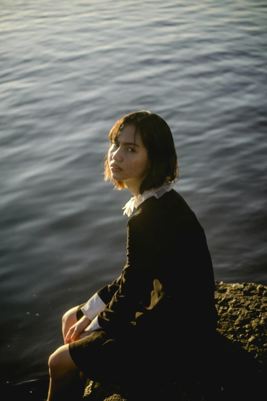 a woman sitting on a rock next to a body of water, inspired by Elsa Bleda, unsplash, realism, with a bob cut, kiko mizuhara, concert, ((portrait))