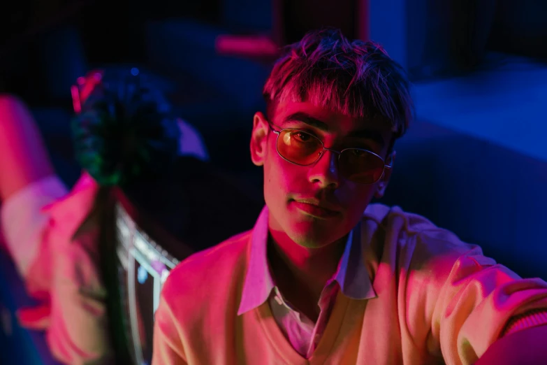 a man sitting at a table with a flower in his hand, an album cover, inspired by Liam Wong, pexels contest winner, neo-fauvism, wearing small round glasses, reflecting light in a nightclub, teenage boy, an epic non - binary model