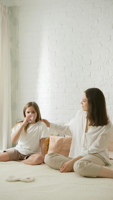 a couple of women sitting on top of a bed, pexels, conceptual art, drinking cough syrup, daughter, at the sitting couch, wearing white pajamas