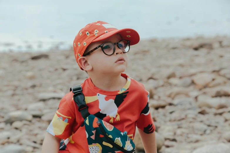 a little boy wearing a hat and glasses, inspired by Leo Leuppi, pexels contest winner, red t-shirt, at the waterside, pokemon cap, patterned clothing