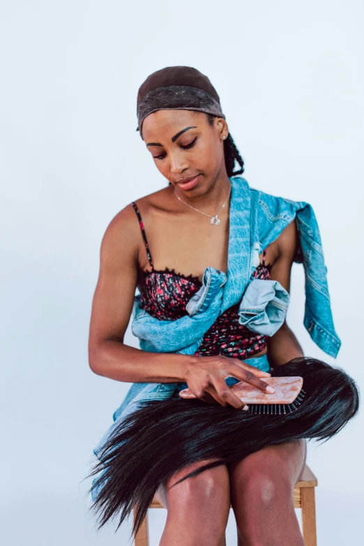 a woman sitting on top of a wooden chair, an album cover, trending on pexels, black arts movement, holding mesh bag with bagels, blue scales covering her chest, playful pose of a dancer, aida muluneh