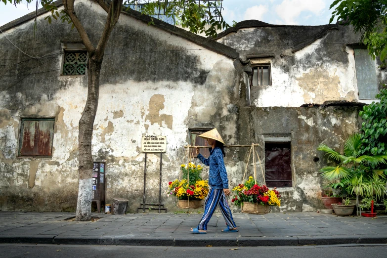 a person walking down a street with a hat on, inspired by Cui Bai, old town, carrying flowers, conde nast traveler photo, an abandoned