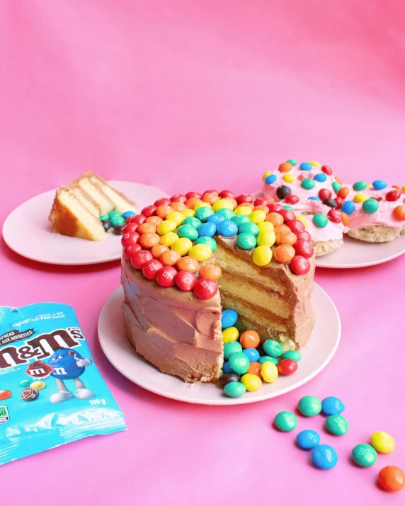 a cake sitting on top of a white plate next to a bag of m & m's, featured on instagram, rainbow stripe backdrop, gemma chen, sherbert sky, layer upon layer